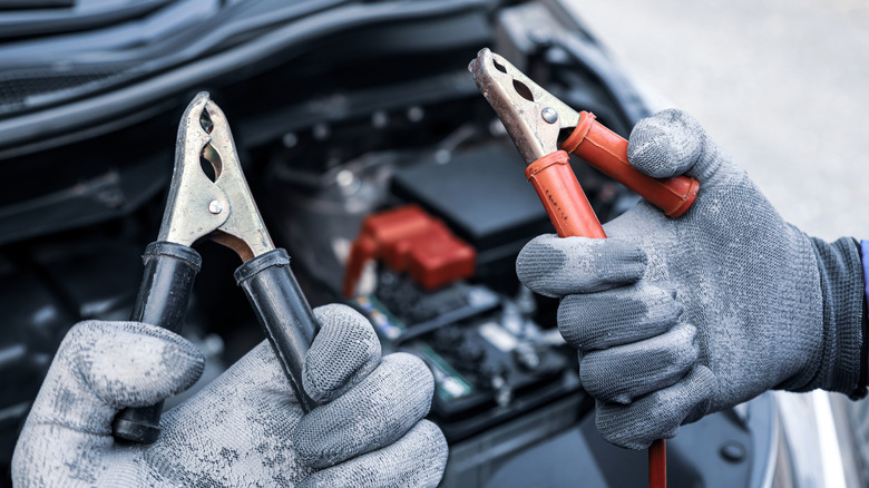 Close up of red and black jumper cables in a mechanic's gloved hands