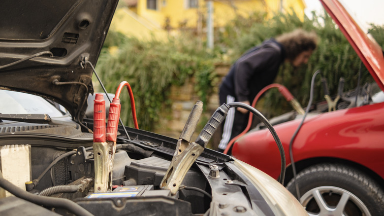 Person jump starting a car, both cars and jump leads partially visible
