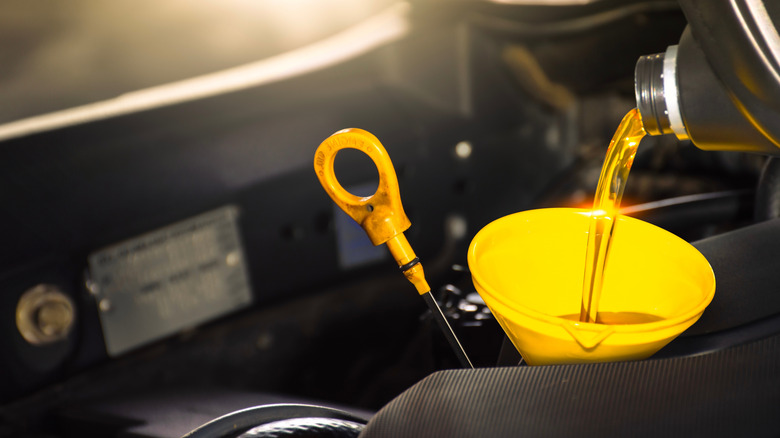 Oil being poured into an engine next to the dipstick