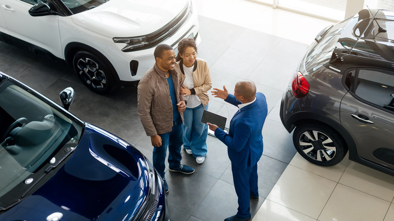 A car dealership salesman speaking with two customers in the showroom
