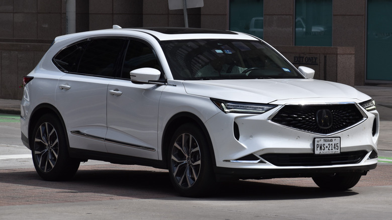 A white Acura MDX driving on a city street