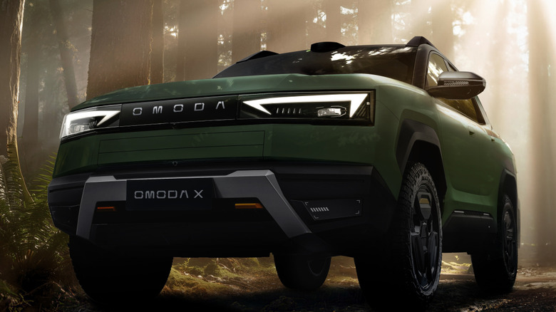 A green Omoda X in the forest, flaunting its jagged LED headlights and aluminum-style skid plate.