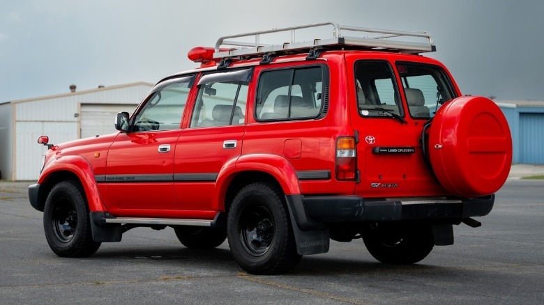 A rear three-quarters view of the Land Cruiser with the custom roof rack and the red spare wheel cover on the tailgate.