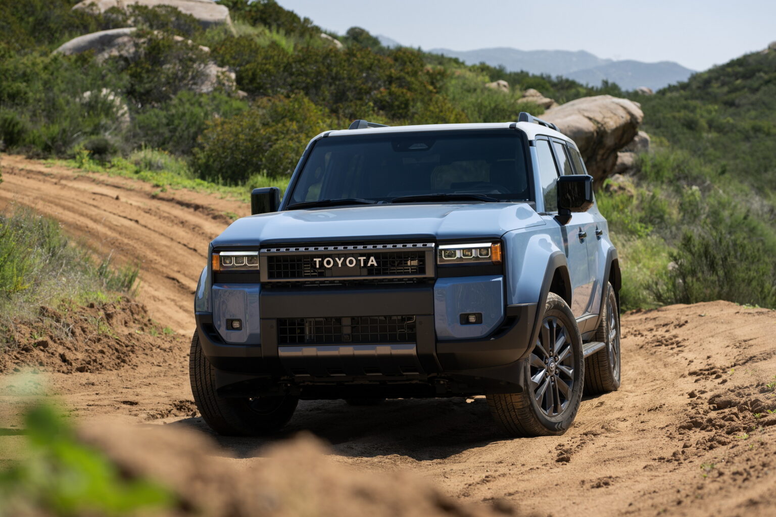 2026 Toyota Land Cruiser front three-quarter in Heritage Blue on a dirt trail